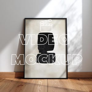 Könnte beinhalten: Schwarz gerahmter Kunstdruck mit einer schwarzen abstrakten Form auf beigem Hintergrund. Die Worte "VIDEO MOCKUP" sind in Weiß überlagert. Der Druck lehnt an einer weißen Wand auf einem Holzboden.