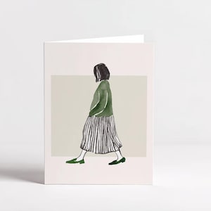 Può includere: Biglietto di auguri con un'illustrazione di una persona con un maglione verde e una gonna a righe. La persona sta camminando, con scarpe verdi. Lo sfondo è di colore neutro e il biglietto è bianco.