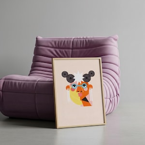 May include: A framed art print featuring a colorful, abstract face design. The artwork includes geometric shapes in orange, yellow, black, and blue, with a light pink background. The print is displayed against a purple armchair.