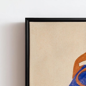May include: A framed artwork featuring a tan canvas with a black frame. The artwork displays a portion of a figure with brown and blue hues. The canvas has a textured appearance, and the frame is a simple, modern design.