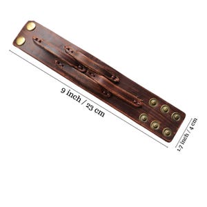 May include: A brown leather cuff bracelet with brass-colored rivets and fasteners. The bracelet is 9 inches (23 cm) long and 1.7 inches (4 cm) wide. The cuff has a distressed appearance.
