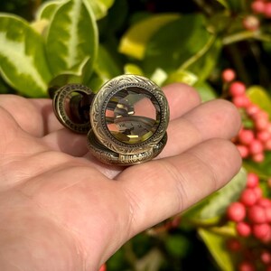 May include: An antique-style pocket watch with an ornate, engraved design. The watch has a clear crystal face, revealing the clock hands and numbers. The watch is a bronze color and appears to be made of metal.