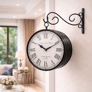 May include: A double-sided, black metal wall clock with a white face and black Roman numerals. The clock is mounted on a decorative black metal bracket. The clock face reads "Village Clock Works" and "Cambridgeshire est. 1796".
