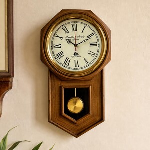 Peut inclure: Une horloge murale octogonale en bois avec une lunette en laiton et un cadran crème orné de chiffres romains noirs. Le cadran porte l'inscription Franklin & Murphy EST 1868 et OXFORD. Un pendule doré est suspendu dans le cadre inférieur.