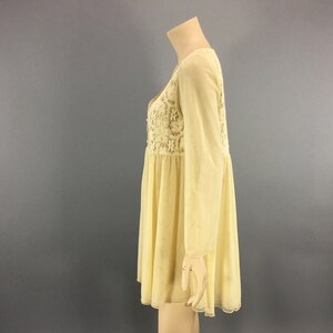 May include: A pale yellow dress with long sleeves and a V-neck. The bodice features intricate floral lace detailing. The dress has a flowing, flared skirt and is displayed on a mannequin against a grey background.