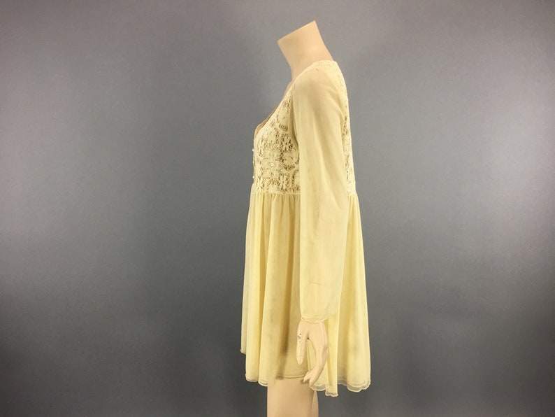 May include: A pale yellow dress with long sleeves and a V-neck. The bodice features intricate floral lace detailing. The dress has a flowing, flared skirt and is displayed on a mannequin against a grey background.