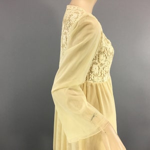 May include: A cream-coloured vintage dress with long, bell sleeves. The bodice features a detailed lace panel, and the dress has a flowing, empire waist silhouette. The fabric appears lightweight and semi-sheer, suggesting a delicate, romantic style.