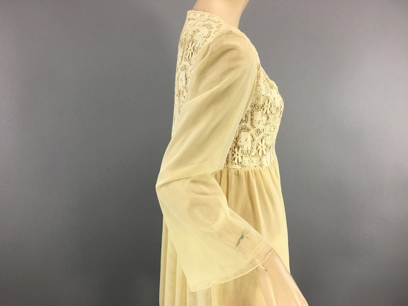 May include: A cream-coloured vintage dress with long, bell sleeves. The bodice features a detailed lace panel, and the dress has a flowing, empire waist silhouette. The fabric appears lightweight and semi-sheer, suggesting a delicate, romantic style.