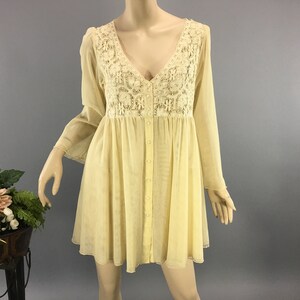 May include: A pale yellow dress with a V-neck and long sleeves. The bodice has a cream lace panel. The dress has a button-down front and a flared skirt. The dress is displayed on a mannequin.