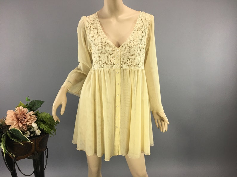 May include: A pale yellow dress with a V-neck and long sleeves. The bodice has a cream lace panel. The dress has a button-down front and a flared skirt. The dress is displayed on a mannequin.