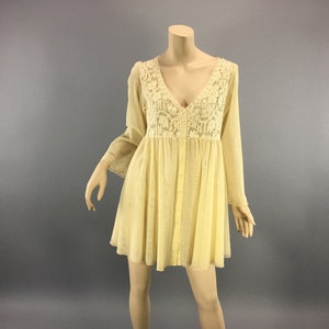 May include: A pale yellow dress with a V-neck and long sleeves. The bodice has a detailed lace panel, and the dress has a button-down front. The dress is displayed on a mannequin. The dress is a mini dress.