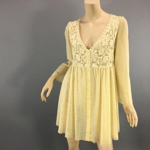 May include: A vintage-style, pale yellow dress with a V-neck and long, flowing sleeves. The bodice has a cream lace panel, and the dress is buttoned down the front. The skirt is short and flared.