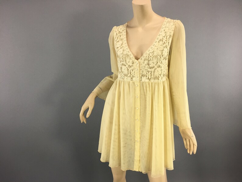 May include: A vintage-style, pale yellow dress with a V-neck and long, flowing sleeves. The bodice has a cream lace panel, and the dress is buttoned down the front. The skirt is short and flared.