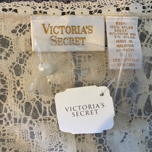 May include: Off-white lace garment with Victoria's Secret tags. The tags display the brand name, material details, and size. The lace features a delicate floral design.