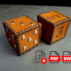 May include: Two handcrafted leather dice in a warm tan color. Each die features stitched edges, silver studs, and black stitching. One die shows the number 5 and 3. A PDF and SVG icon are in the bottom right corner.