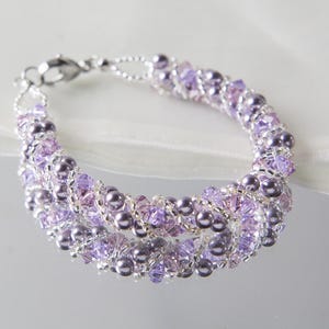 May include: A delicate bracelet featuring multiple strands of lavender and silver beads. The bracelet is adorned with small, sparkling crystals and larger, round beads, creating a layered effect. The clasp is silver.