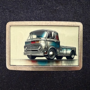 May include: A rectangular metal belt buckle featuring a vintage truck illustration. The truck is primarily blue and silver, with red and blue accents. The buckle has a silver frame and a cream-colored background.