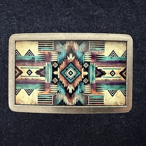 May include: Rectangular metal belt buckle with a Southwestern geometric design. The design features a central diamond shape surrounded by teal, purple, and tan patterns. The buckle has a silver-colored frame.
