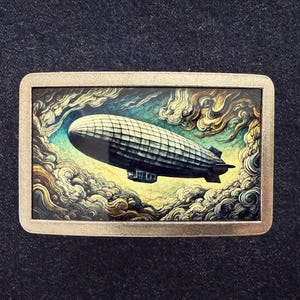 May include: A rectangular metal belt buckle featuring a vintage illustration of a zeppelin airship. The airship is depicted in a detailed, artistic style, set against a backdrop of swirling clouds in shades of blue, yellow, and brown.