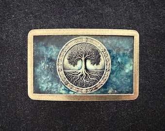 May include: Rectangular belt buckle with a detailed tree of life design. The tree is in a circular frame with an ornate border, set against a teal and blue background. The buckle has a gold-colored frame.