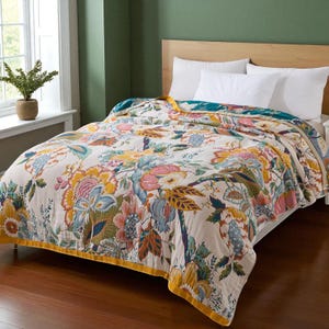May include: A cream-coloured quilt with a vibrant floral pattern in pink, yellow, blue, and green. The quilt, edged with yellow, is displayed on a bed with white pillows. The quilt's design includes large, detailed blooms.