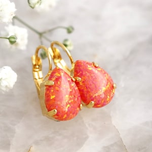 May include: A pair of gold hoop earrings with teardrop-shaped pink opal stones. The earrings are on a white background.