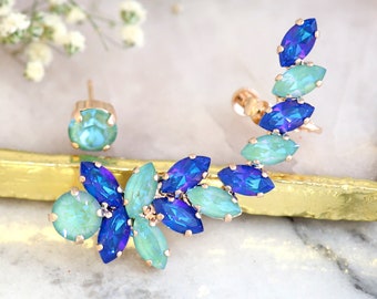 Puede incluir: Un par de pendientes de aro con adornos de cristal azul y verde. Los pendientes de aro son de metal dorado.