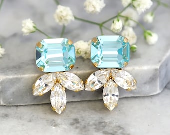 May include: A pair of earrings featuring a large, rectangular, light blue faceted crystal set in gold-tone metal, with three smaller, clear, marquise-cut crystals arranged in a fan shape beneath each main stone.