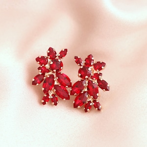 May include: A pair of red crystal earrings with a floral design. The earrings are made of gold-toned metal and have a cluster of red crystals in the shape of flowers.