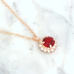 May include: A rose gold necklace with a red gemstone pendant surrounded by a halo of smaller clear gemstones.