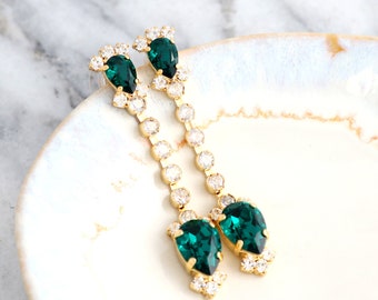 May include: A pair of long, gold dangle earrings with emerald green and clear crystal stones.