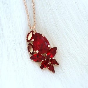 Può includere: Una collana con catena dorata con un ciondolo che presenta un gruppo di pietre di cristallo rosse.