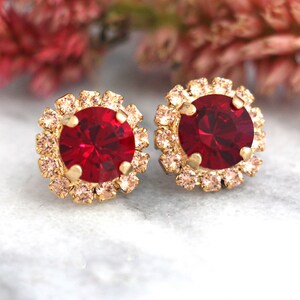 Puede incluir: Un par de pendientes de oro con un centro de cristal rojo rodeado por un halo de cristales rosas más pequeños.