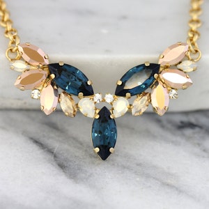 May include: A gold chain necklace with a statement pendant featuring a cluster of marquise-shaped crystals in shades of blue, pink, and white.