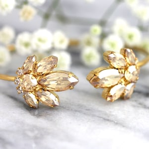 May include: A gold bracelet with a delicate design featuring a cluster of clear and champagne-colored crystals. The bracelet is open and has a simple, elegant style.