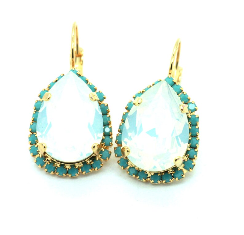 May include: A pair of gold teardrop earrings with a large clear teardrop crystal surrounded by a halo of turquoise crystals.