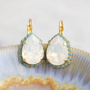 May include: A pair of gold teardrop earrings with a white opal stone and a light blue crystal border.