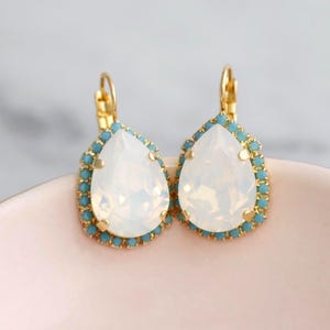May include: A pair of gold teardrop earrings with a white opal stone and a blue crystal halo.