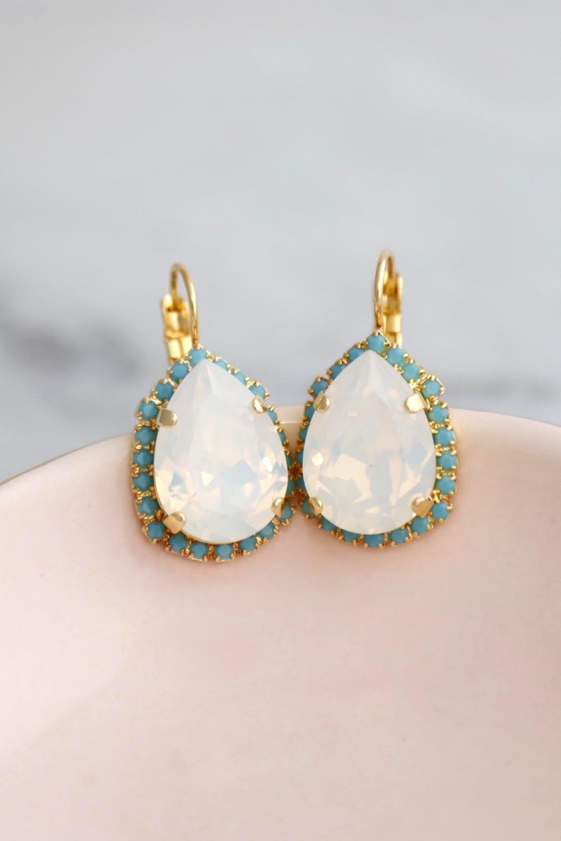May include: A pair of gold teardrop earrings with a white opal stone and a blue crystal halo.