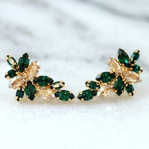 Puede incluir: Un par de pendientes dorados con un diseño floral. Cada pendiente está adornado con cristales verdes esmeralda y champán con corte marquesa. Los cristales están engastados en una montura de metal dorado.