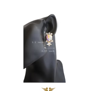 May include: A pair of gold skull earrings with colorful enamel and clear rhinestones. The earrings are 1.1 inches tall and 0.57 inches wide.