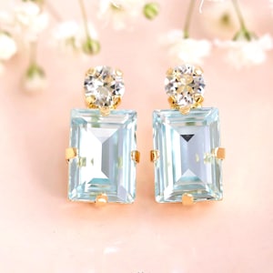 Puede incluir: Un par de pendientes de oro con cristales cuadrados de color azul claro y cristales redondos transparentes. Los pendientes están adornados con cristales de Swarovski.