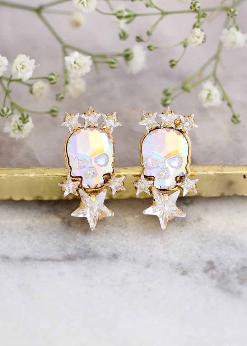 May include: A pair of gold-tone earrings featuring a crystal skull with a rainbow iridescent finish and a cluster of clear crystal stars.