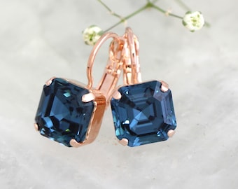 May include: Rose gold earrings with a square blue gemstone. The earrings have a lever back closure.