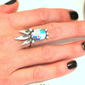 Puede incluir: Un anillo de plata con un dise&ntilde;o de calavera de cristal. El anillo est&aacute; en un dedo con esmalte de u&ntilde;as negro.