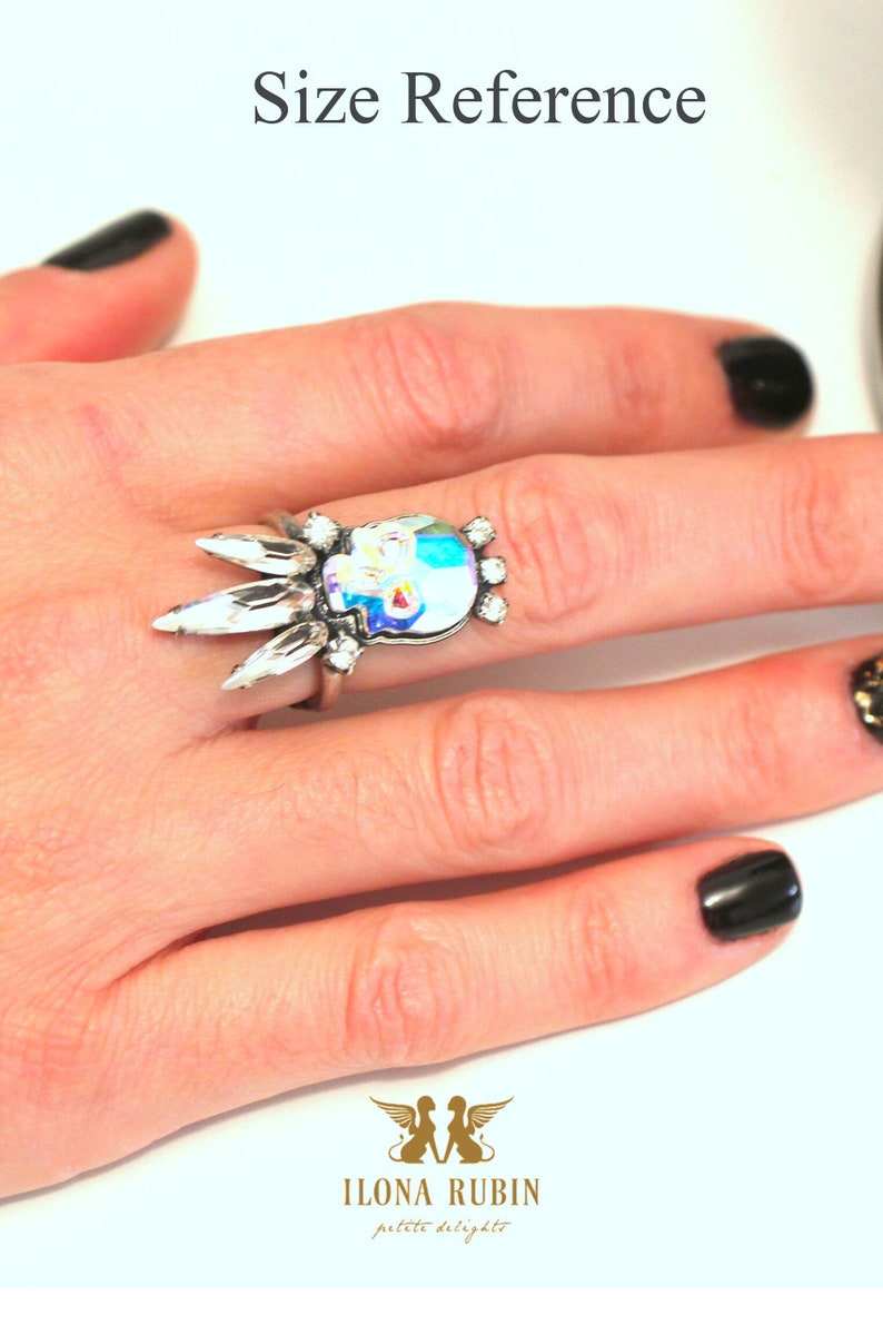 Puede incluir: Un anillo de plata con un dise&ntilde;o de calavera de cristal. El anillo est&aacute; en un dedo con esmalte de u&ntilde;as negro.