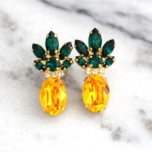Könnte beinhalten: Ein Paar goldene Ananas-Ohrringe mit grünen und gelben Kristall-Akzenten.