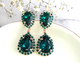 May include: A pair of emerald green teardrop-shaped earrings with a smaller emerald green stone at the top. The earrings are set in rose gold and have a halo of smaller emerald green stones around each stone.