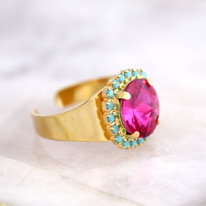 May include: A gold ring with a large pink gemstone surrounded by a halo of turquoise stones.