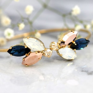 May include: A gold bangle bracelet with a cluster of blue, white, and pink crystal stones in a flower shape.